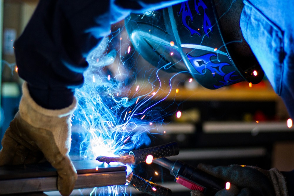Welder in protective gear joining steel, the arc lighting the work in blue