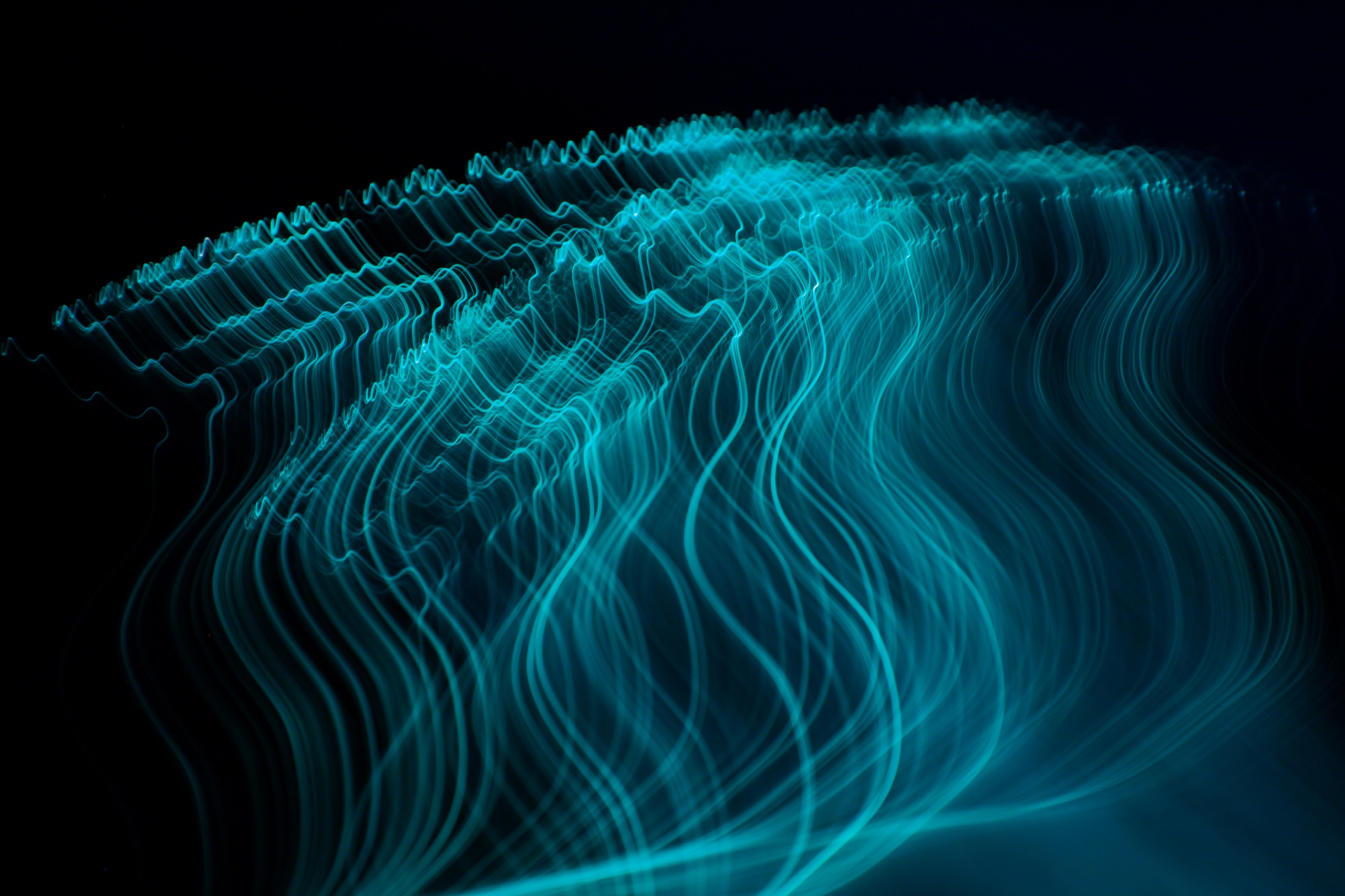 Long-exposure trails of teal light flowing across a dark background