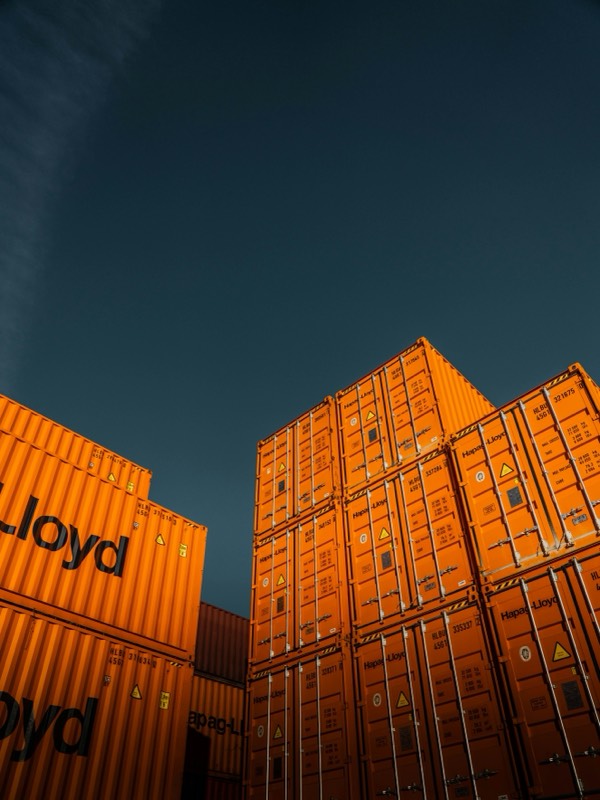 Stacked orange shipping containers against an evening sky